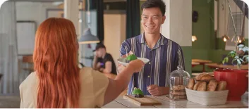 A learner being handed food across a café counter by a smiling server