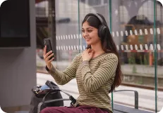 A learner at a bus stop speaking into her phone, wearing headphones